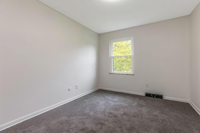 spare room with baseboards, dark carpet, and visible vents
