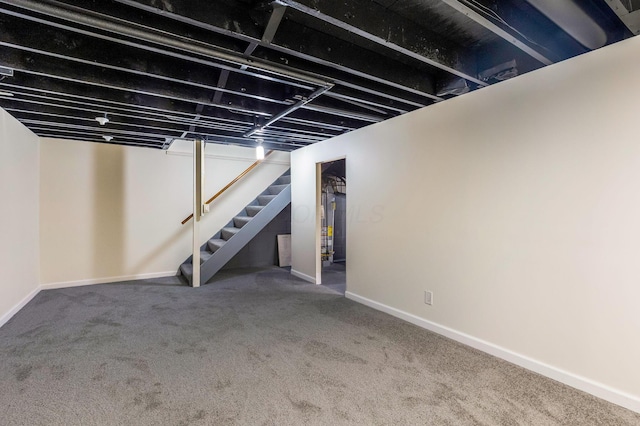 finished basement with carpet floors, baseboards, gas water heater, and stairway
