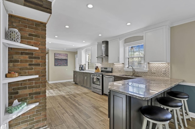 kitchen featuring light stone counters, stainless steel appliances, white cabinets, a sink, and wall chimney exhaust hood