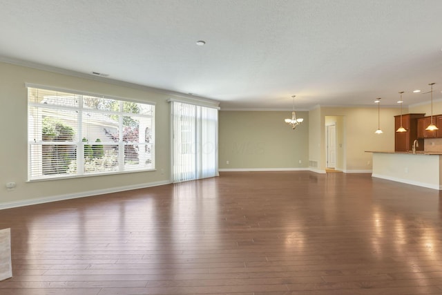 unfurnished living room with an inviting chandelier, crown molding, visible vents, dark wood-style floors, and a sink