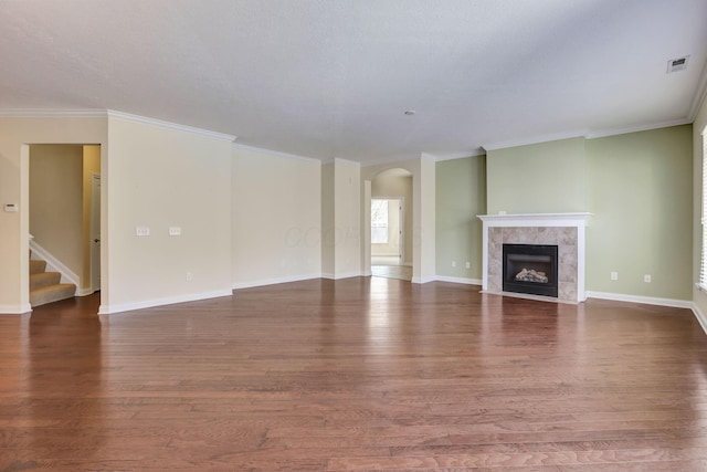 unfurnished living room with visible vents, crown molding, arched walkways, a tile fireplace, and wood finished floors