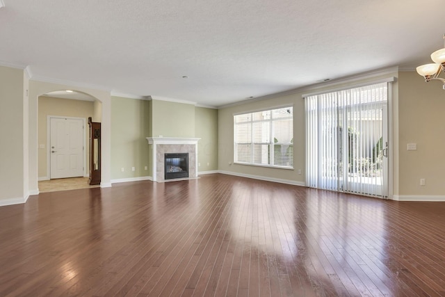 unfurnished living room featuring a fireplace, arched walkways, baseboards, ornamental molding, and hardwood / wood-style flooring