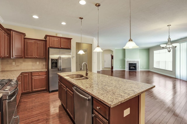 kitchen featuring light stone countertops, a sink, open floor plan, ornamental molding, and stainless steel appliances