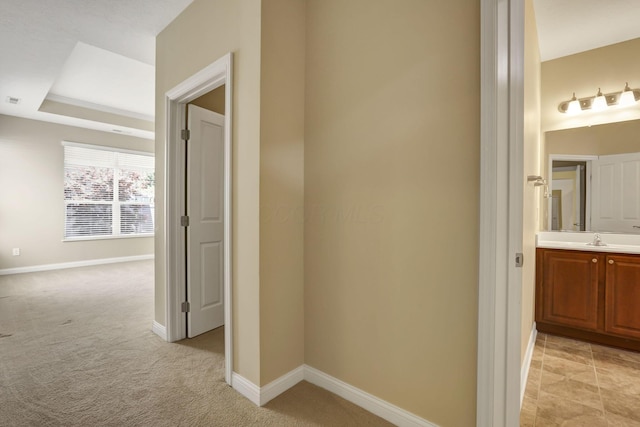 hall featuring a sink, baseboards, and light carpet