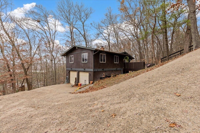 view of home's exterior with dirt driveway, a deck, a chimney, and a garage