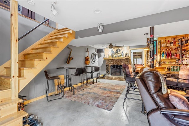 living area featuring stairway, a ceiling fan, finished concrete floors, and a brick fireplace