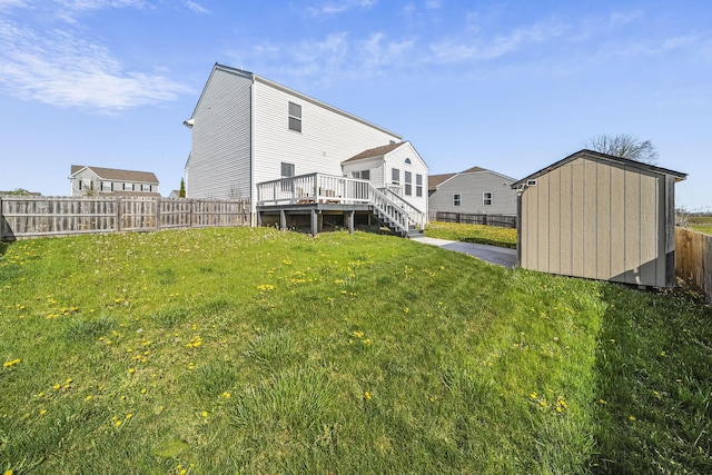back of property with a lawn, a wooden deck, an outbuilding, a fenced backyard, and a storage unit
