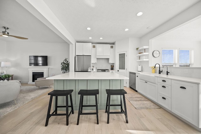 kitchen featuring open shelves, appliances with stainless steel finishes, a sink, white cabinetry, and a kitchen island