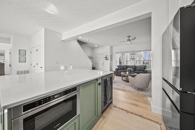 kitchen with ceiling fan, light stone counters, wine cooler, green cabinetry, and light wood-style flooring