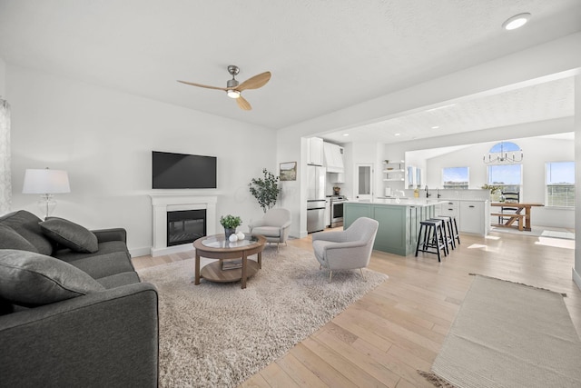 living area with light wood-style floors, recessed lighting, a glass covered fireplace, and ceiling fan