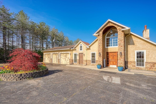 view of front of home with driveway, a chimney, stone siding, and stucco siding