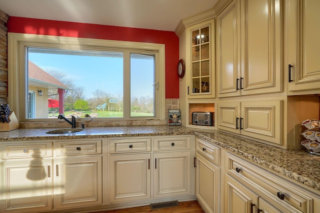 kitchen with visible vents, light stone countertops, glass insert cabinets, cream cabinets, and a sink