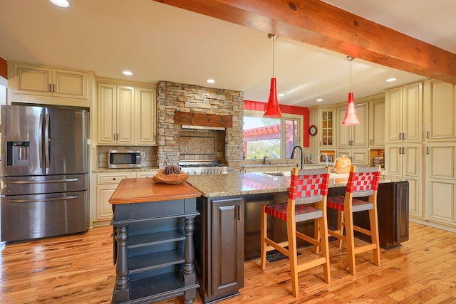 kitchen featuring a large island with sink, light wood-style flooring, cream cabinets, and stainless steel appliances