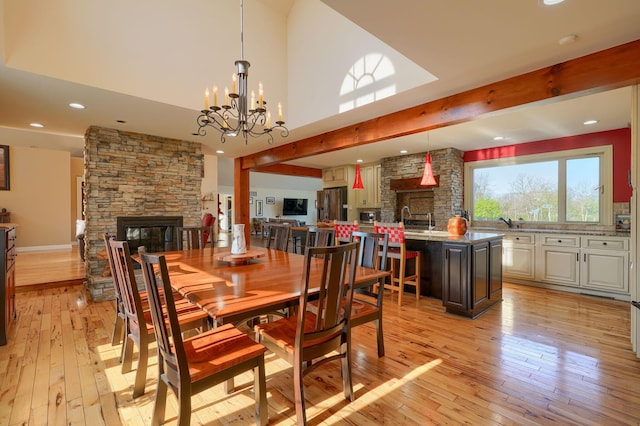 dining room with a notable chandelier, a stone fireplace, light wood-style flooring, recessed lighting, and a towering ceiling