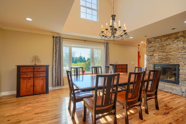 dining space featuring an inviting chandelier, a stone fireplace, recessed lighting, light wood-type flooring, and ornamental molding