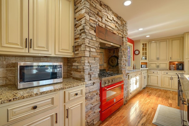 kitchen with light wood-type flooring, cream cabinetry, light stone counters, backsplash, and stainless steel appliances