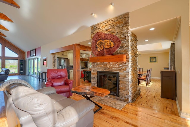 living room featuring a stone fireplace, high vaulted ceiling, baseboards, recessed lighting, and light wood-style flooring