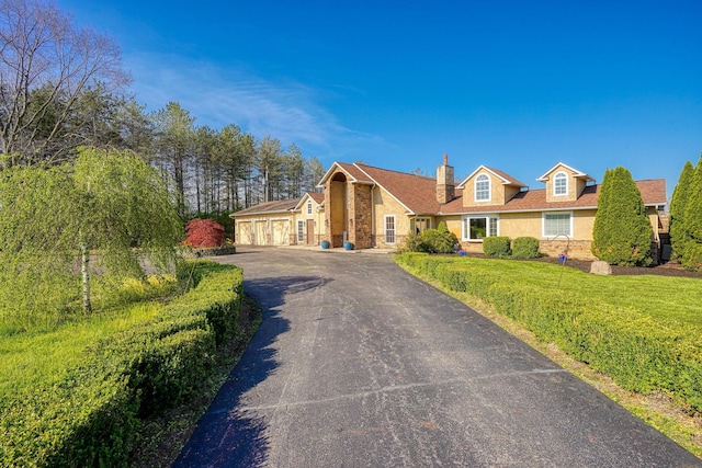 view of front facade featuring a chimney, driveway, a front lawn, and stone siding
