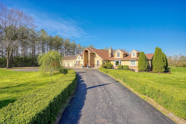 cape cod home with aphalt driveway, a chimney, and a front lawn