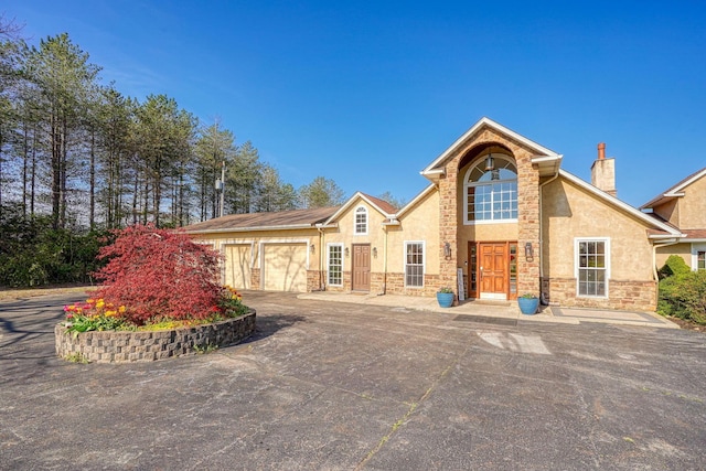 view of front of home with a garage, stucco siding, a chimney, and aphalt driveway