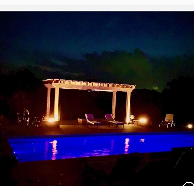 pool at night featuring a pergola, a patio area, and an outdoor pool