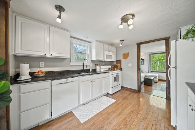 kitchen with dark countertops, white appliances, light wood-style floors, white cabinets, and a sink