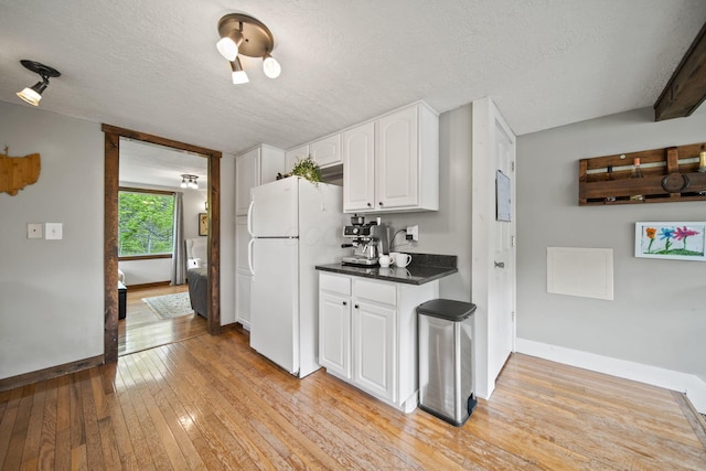 kitchen with dark countertops, a textured ceiling, light wood-style flooring, freestanding refrigerator, and white cabinetry