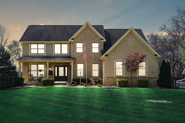 view of front of property featuring stucco siding, a front yard, stone siding, and covered porch