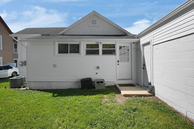 rear view of house with a shingled roof, central air condition unit, and a yard