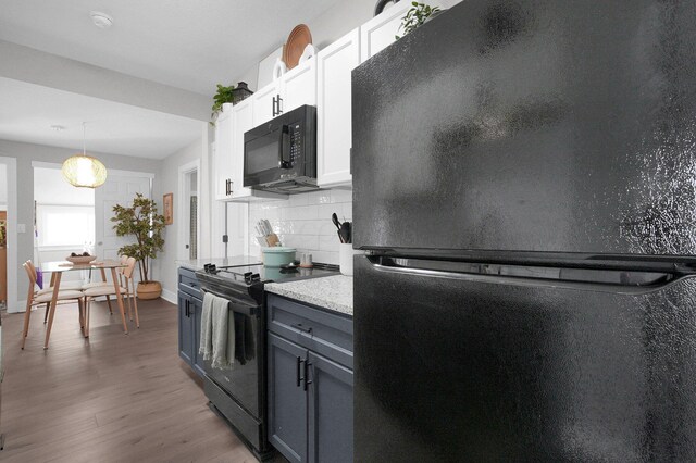 kitchen featuring hanging light fixtures, light countertops, wood finished floors, tasteful backsplash, and black appliances