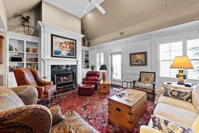 living area with ceiling fan, visible vents, wood finished floors, a tiled fireplace, and high vaulted ceiling