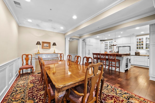 dining space featuring crown molding, a decorative wall, visible vents, dark wood-style flooring, and wine cooler