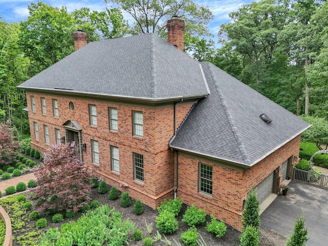 view of home's exterior with brick siding, a shingled roof, driveway, and a chimney