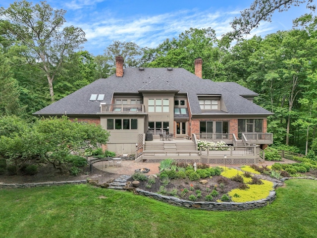 rear view of house with a lawn, a chimney, a patio area, and a balcony