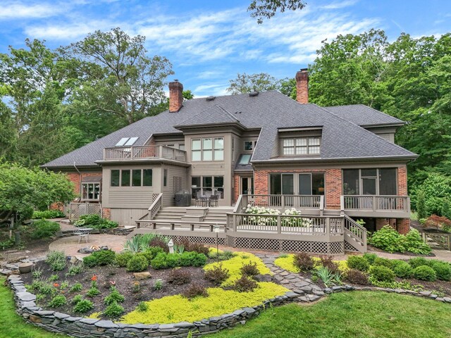 rear view of house featuring stairs, a chimney, a balcony, and brick siding