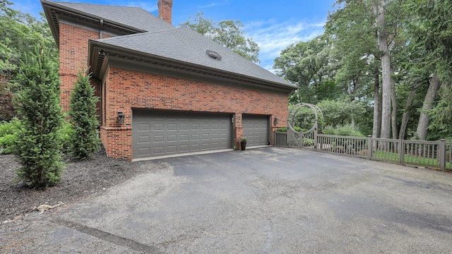 view of property exterior featuring roof with shingles, a chimney, aphalt driveway, and brick siding