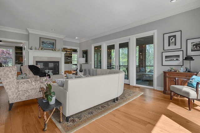 living room with crown molding, recessed lighting, a glass covered fireplace, and light wood-type flooring