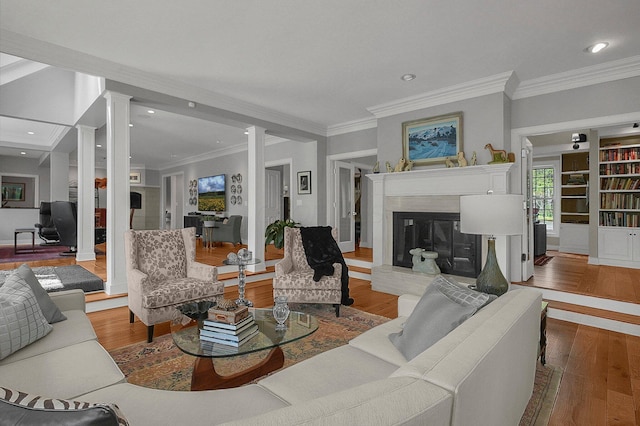living room with crown molding, decorative columns, a glass covered fireplace, and wood finished floors