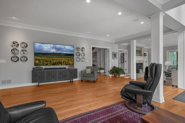 living area featuring crown molding, a fireplace, light wood-style flooring, ornate columns, and visible vents
