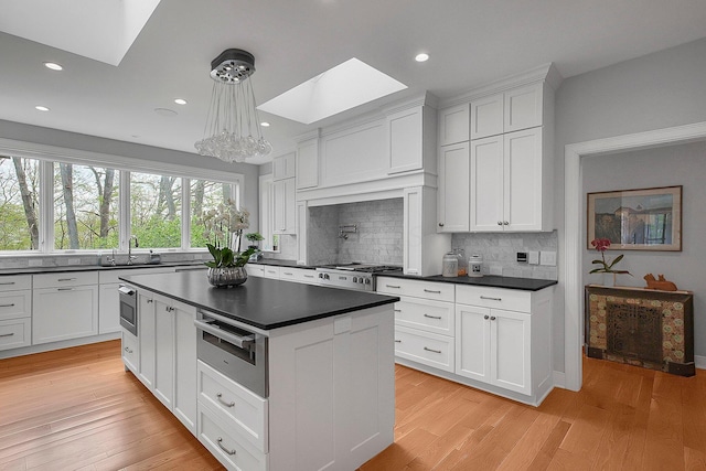 kitchen with white cabinets, dark countertops, an inviting chandelier, backsplash, and a skylight