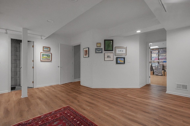 below grade area with baseboards, light wood-type flooring, rail lighting, and visible vents