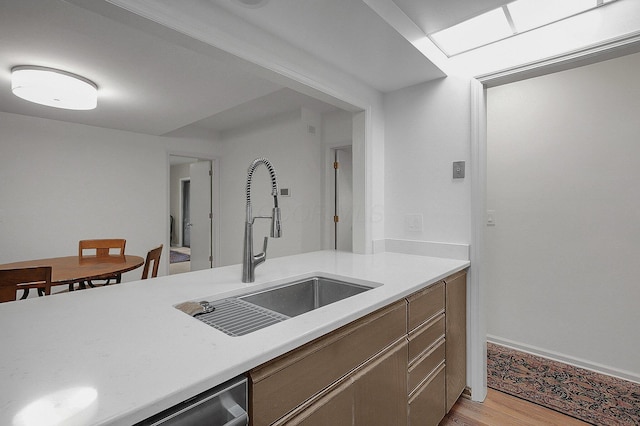 kitchen featuring a sink, light countertops, baseboards, and light wood-style floors