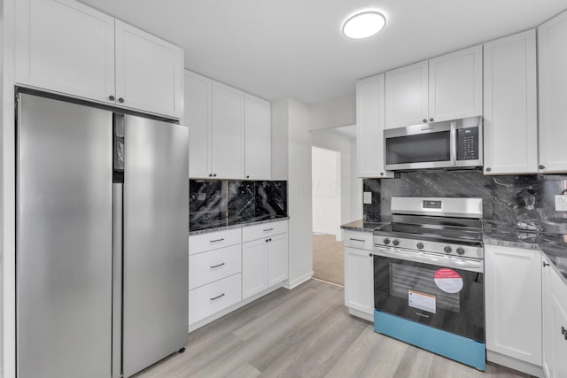 7847 Maplecreek Ct, Powell, OH 43065 - kitchen featuring white cabinets, appliances with stainless steel finishes, light wood-style flooring, dark stone countertops, and backsplash