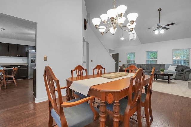 dining space with high vaulted ceiling, dark wood-style floors, a wealth of natural light, and ceiling fan with notable chandelier