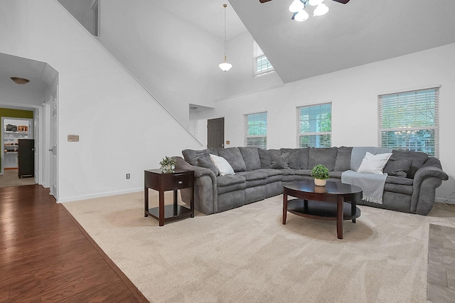 living room featuring baseboards, a ceiling fan, a towering ceiling, and wood finished floors