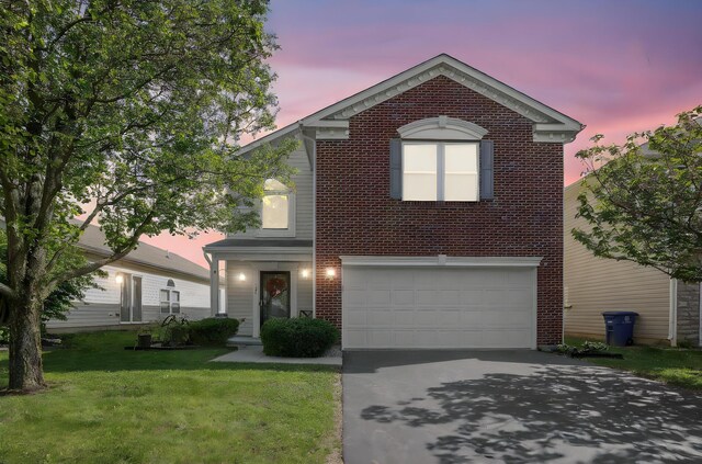 traditional-style house featuring an attached garage, aphalt driveway, a yard, and brick siding