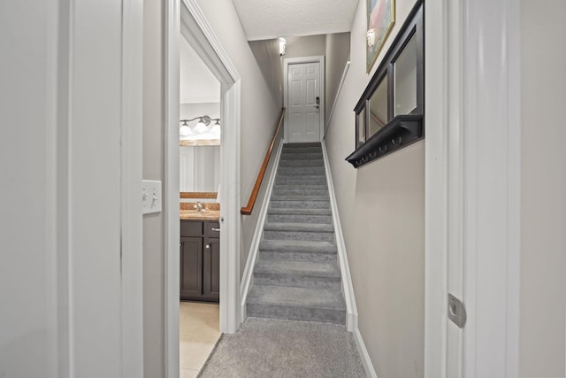 stairs featuring a textured ceiling, baseboards, and carpet