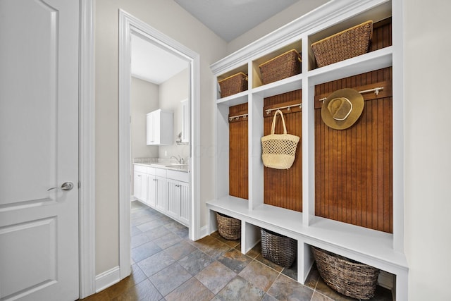 mudroom with baseboards, stone finish floor, and a sink