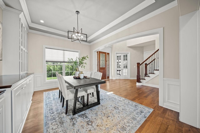 dining space with an inviting chandelier, arched walkways, stairs, wood finished floors, and ornamental molding
