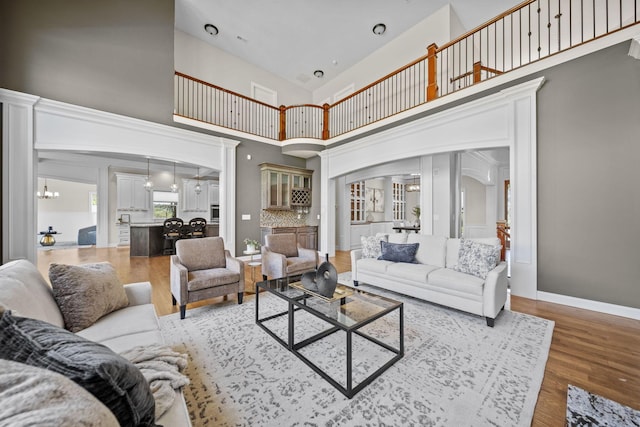 living room featuring an inviting chandelier, arched walkways, light wood finished floors, and a high ceiling
